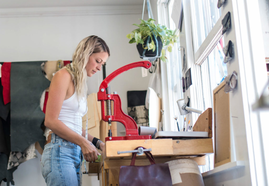 Fashion designer Gina deWolfei in jeans and tank working with leather in her accessories store