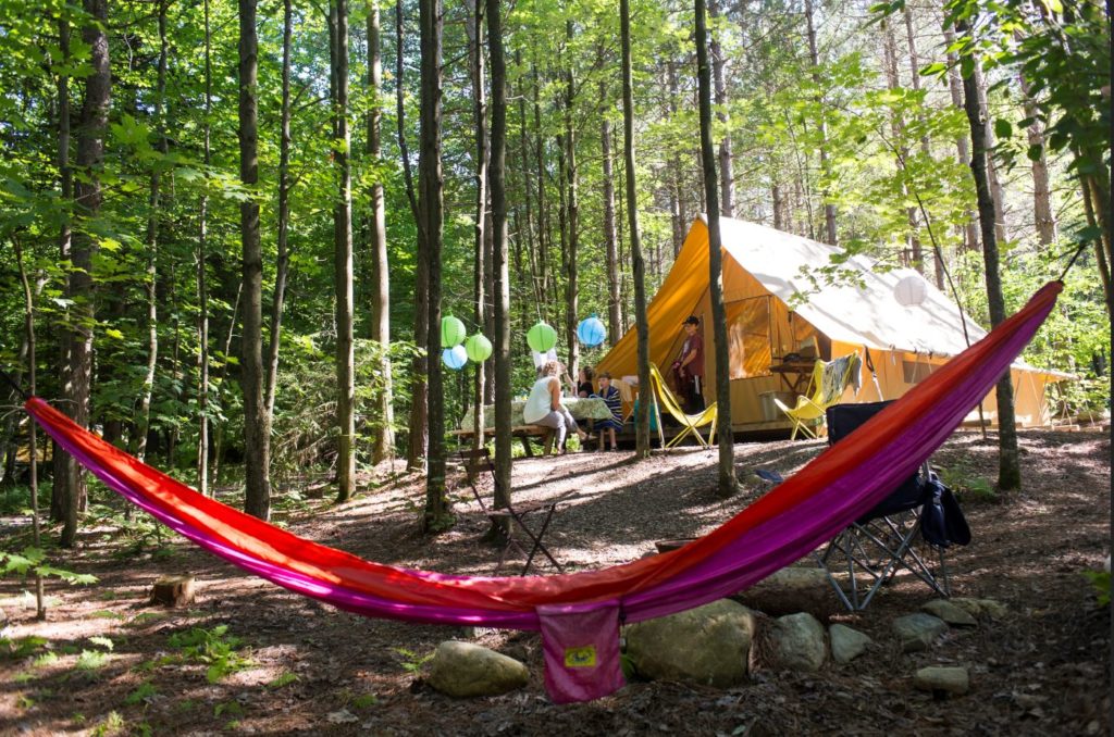 A colorful hammock, picnic table, and outdoor seating in front of a tent at Huttopia 