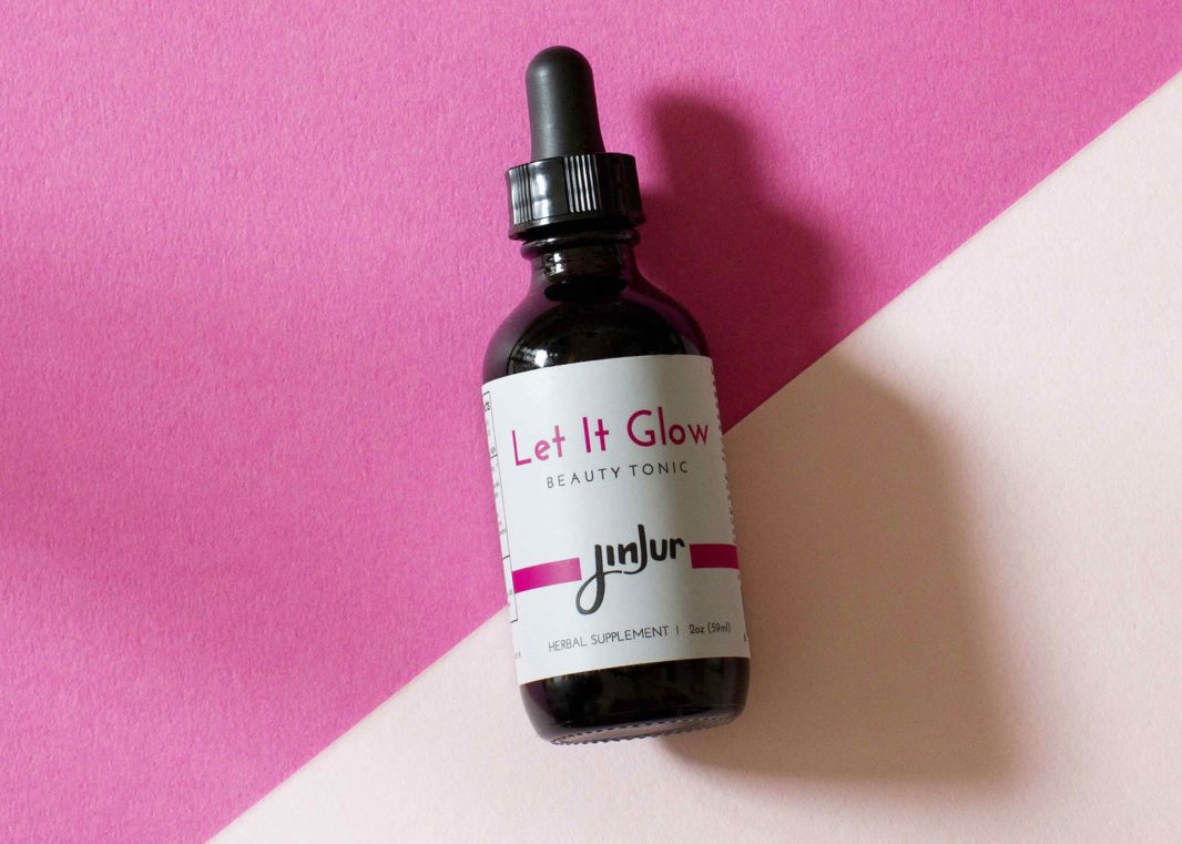 Jinjur Let It Glow Beauty Tonic dropper bottle on two-tone pink diagonal pattern background 