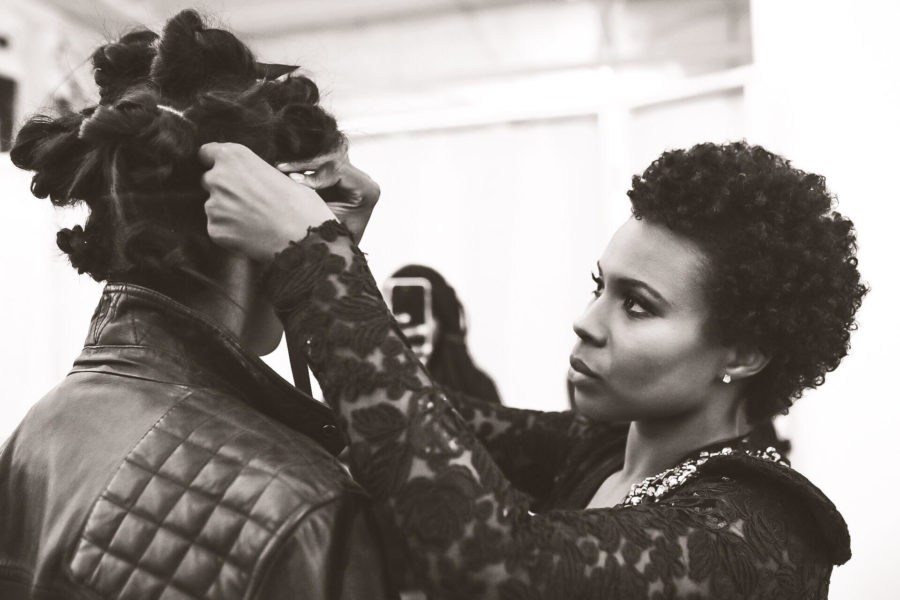 Black and white photo of fashion designer Joelle Jean-Fontaine making adjustments to a model wearing her I Am Kréyol designs