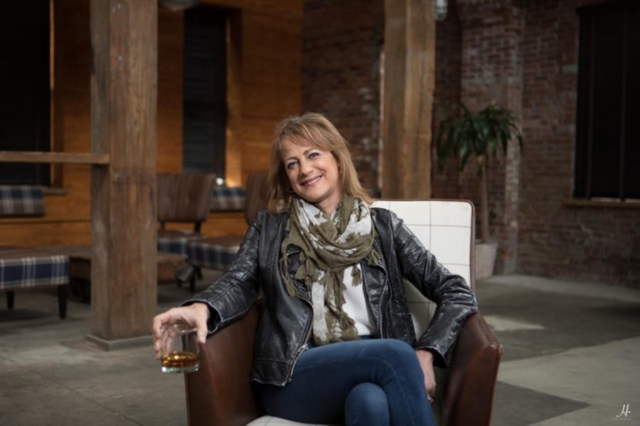 Boston Harbor Distillery founder Rhonda Kallman sitting in leather chair in leather jacket and scarf with glass of whiskey