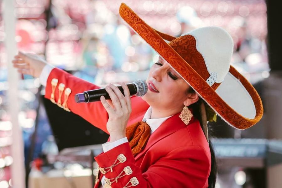 Veronica Robles singing in a red and white sombrero and red mariachi jacket with gold buttons