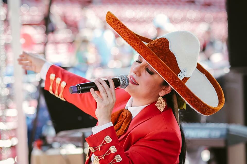 Veronica Robles singing in a red and white sombrero and red mariachi jacket with gold buttons