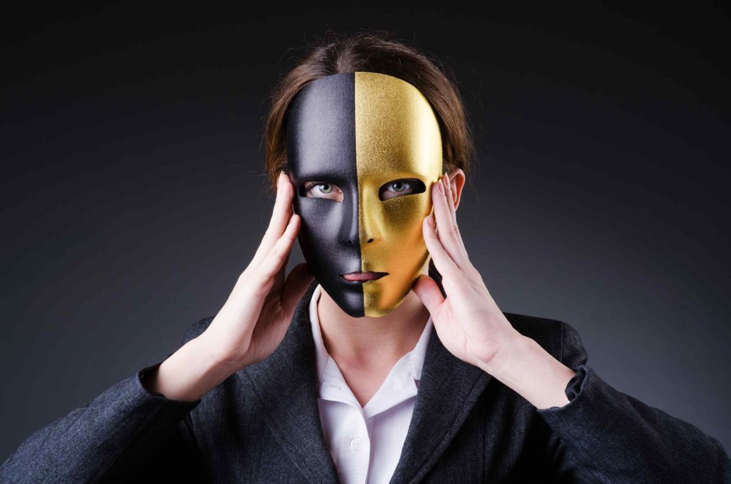 Woman in blazer holding half black half gold mask over her face
