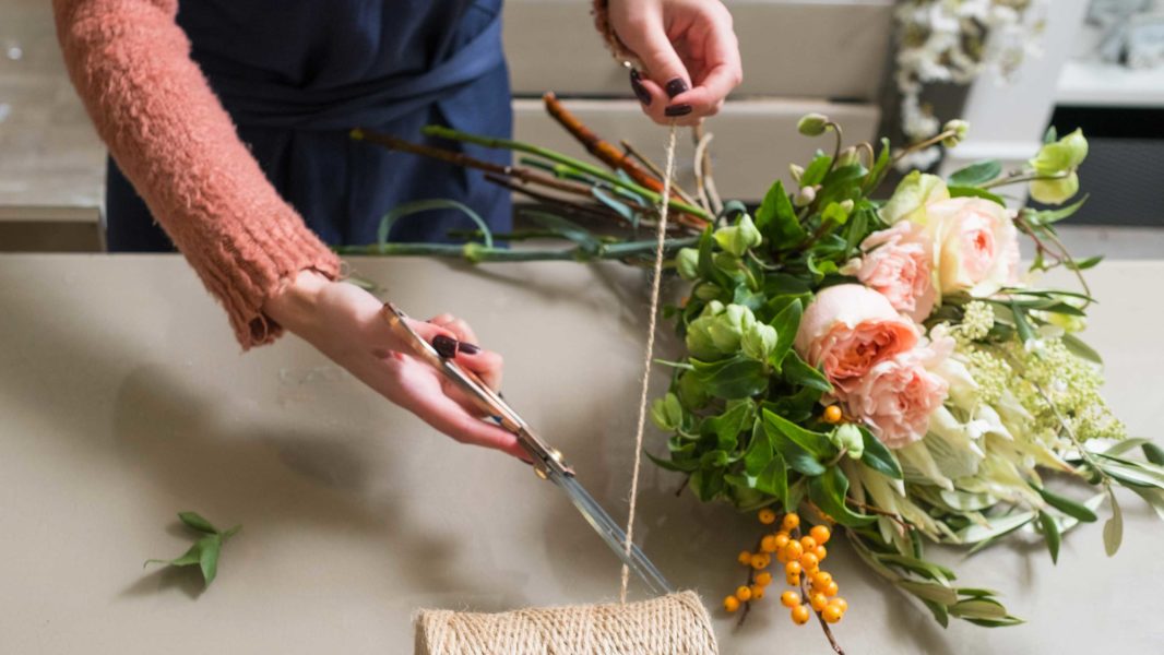 woman cutting twine to tie around a fresh bouquet of flowers including light pink roses
