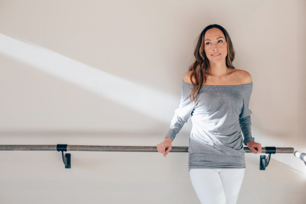 Jessica Diaz at the barre in a grey off-the-shoulder top and white pants