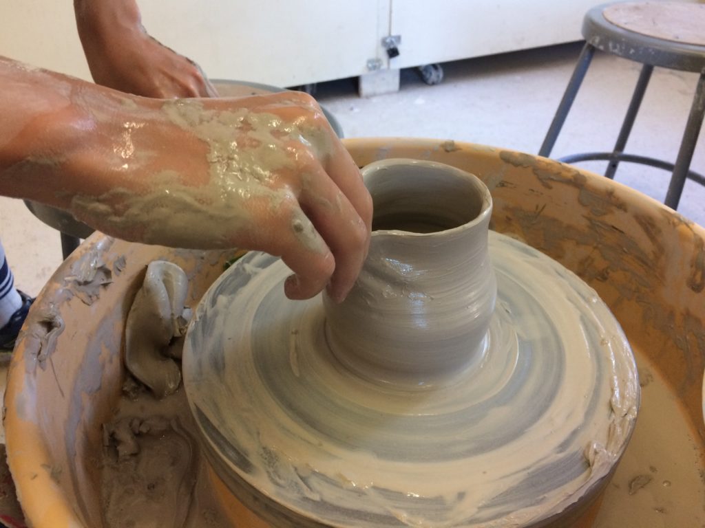 hands making a clay pot on a spinning pottery wheel