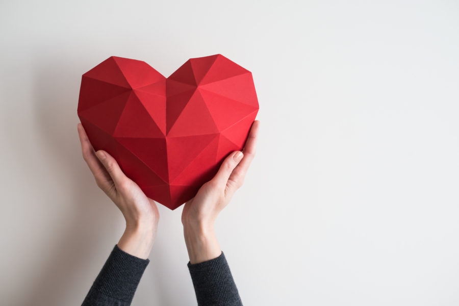 woman's arms holding red heart with origami-style fold marks