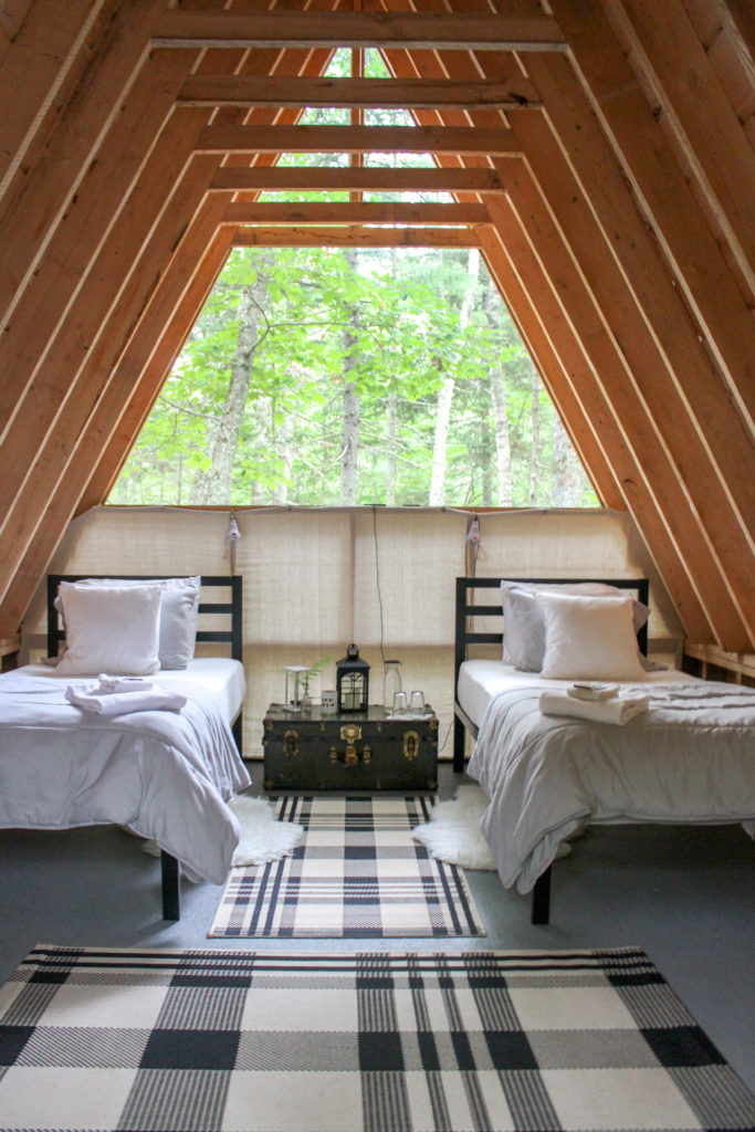 The rustic-chic interior of a Tops’l Farm cabin with two twin beds and modern plaid carpet
