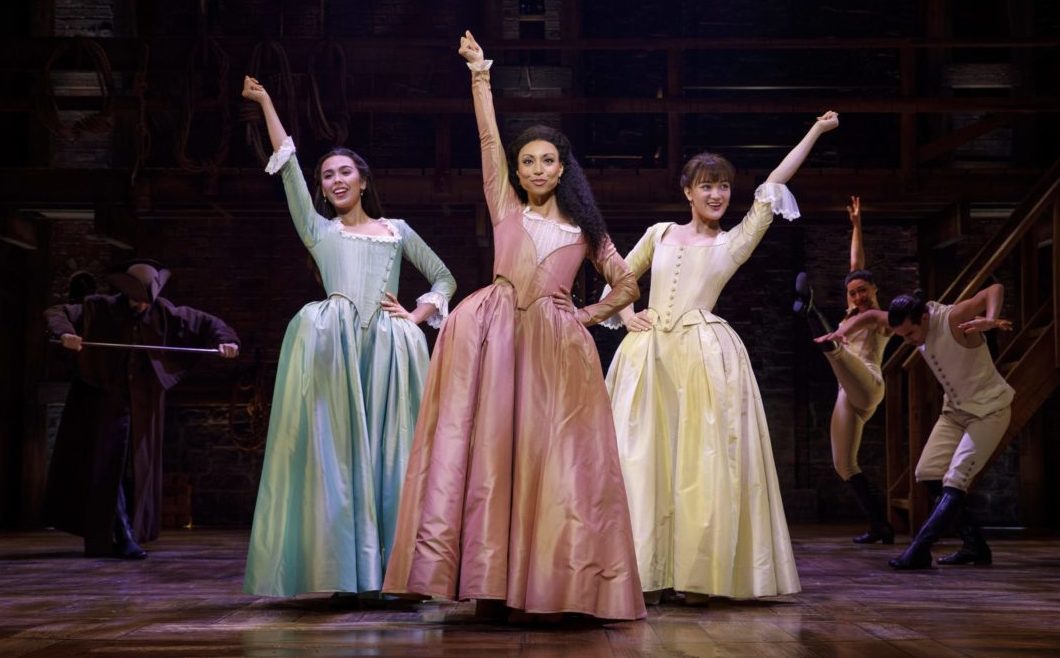 Stage actresses Julia K Harriman, Sabrina Sloan, and Isa Briones in pouffy pastel-colored period costume dresses in the Hamilton musical in Boston