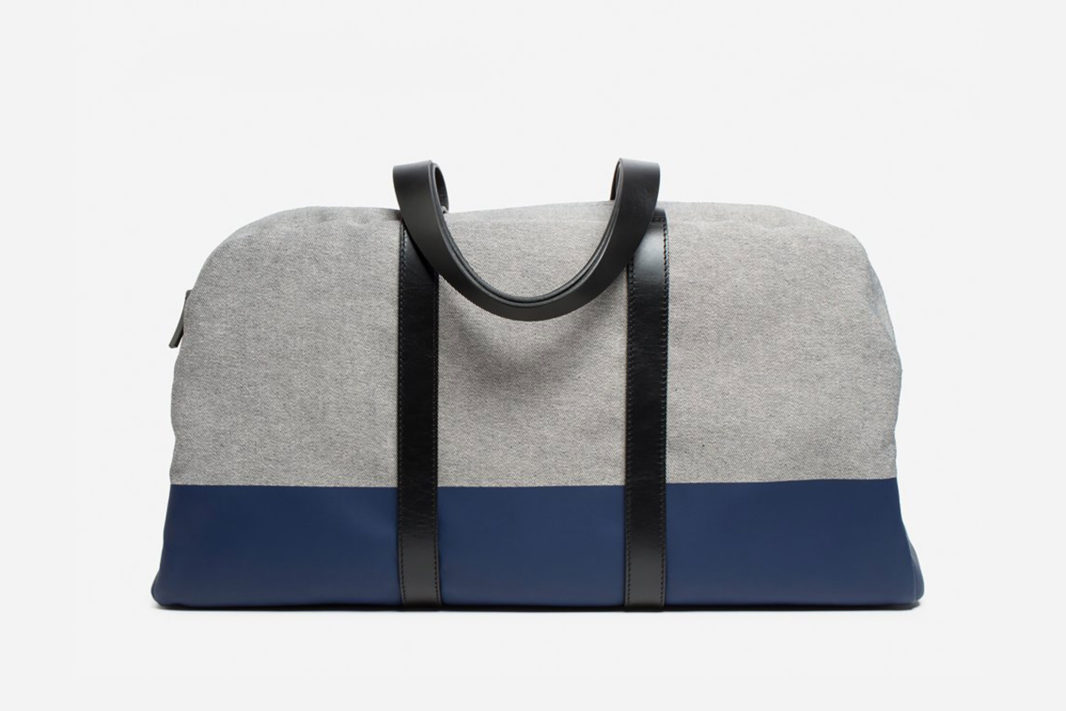 Everlane The Twill Weekender duffle bag in grey with navy bottom and black leather straps.